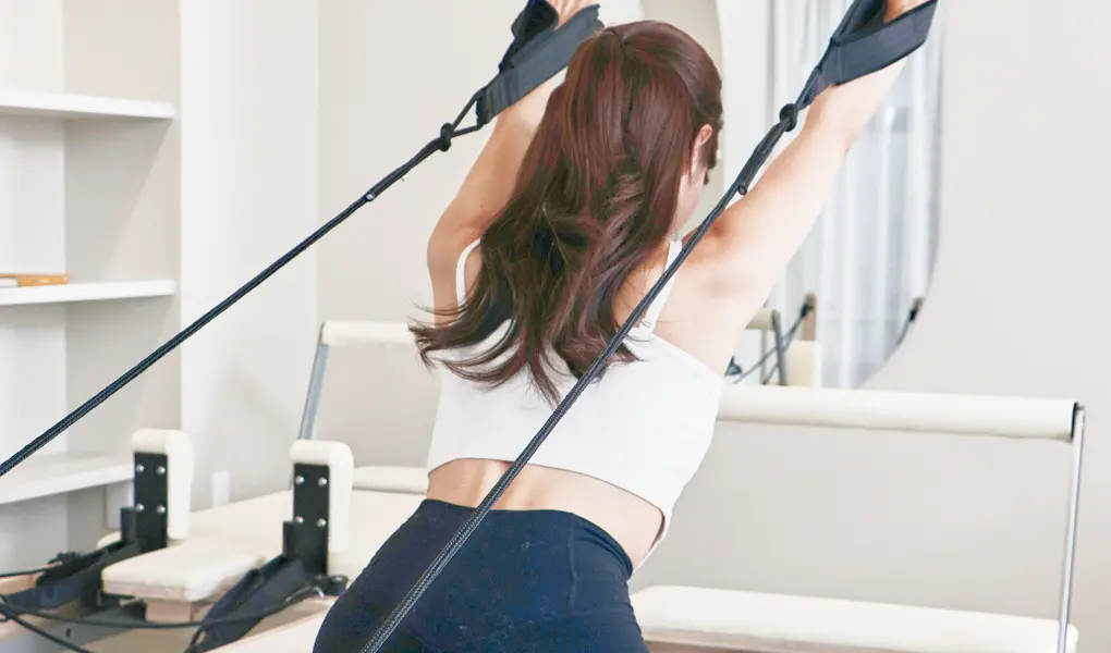 ピラティスマシンで女性が上半身のストレッチをしている様子